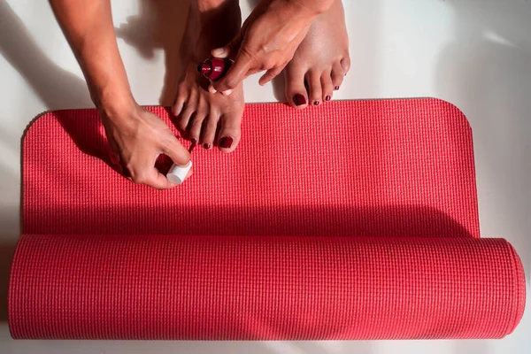 De dessus de la culture femelle anonyme faisant pédicure et appliquant vernis à ongles sur tapis de yoga à la maison — Photo de stock