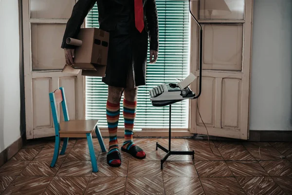 Schnappschuss eines Mannes mit Kartonmaske in gestreiften Socken, der neben einer Retro-Schreibmaschine steht — Stockfoto