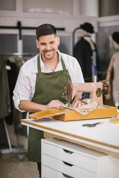 Alfaiate masculino focado em detalhes de roupas de costura de avental usando máquina de costura moderna à mesa enquanto cria coleção de roupas exclusivas no estúdio de trabalho contemporâneo — Fotografia de Stock