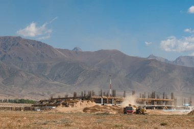 Bir kazıcı, Kırgızistan 'daki yeni Tamchy Havaalanı binasının arkaplanına toprak dolu bir çöp kamyonu yüklüyor..
