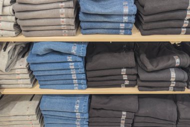 Mağazalarda çeşitli boyutlarda pantolon ve kot pantolon yığınları var..