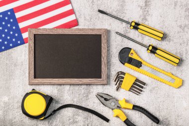 Tahta çerçeve, boş siyah maket, inşaat aletleri ve beton arka planda Amerikan bayrağı. İşçi Bayramı, 1 Mayıs, Babalar Günü konsepti..