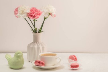 Kahve, makarna ve pembe karanfiller beyaz bir masada. Kadın masası. Sıcak kahvaltı..