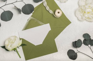 Kadınsı davetiye veya yeşil zarflı tebrik kartı modeli, hediye kutusu ve beyaz şakayık çiçekleri, okaliptüs dalları ve açık arkaplanda açılış kurdelesi. Boş kartpostal.