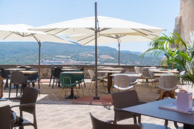 Dışarıdaki terasta şemsiyelerin altında masalar ve sandalyeler manzaralı bir dağ manzarası. Yemek veya dinlenmek için ideal bir ortam, çeşitli faaliyetler için sakin bir ortam sağlar..