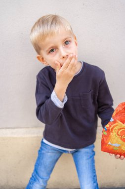 Açık havada patlamış mısır yiyen mavi gözlü sevimli çocuk. Çocukluk sevinci, ikramlar, abur cubur, boş zaman ve yaşam tarzı kavramı