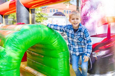 Gülümseyen çocuk dışarıda şişme oyun alanının tadını çıkarıyor. Çocukluk keyfi, eğlence parkı aktivitesi, eğlence, eğlence ve aile hafta sonu eğlencesi kavramı.