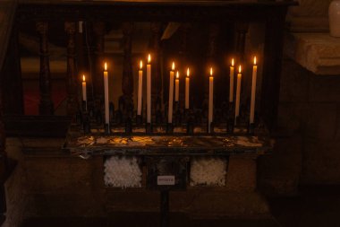 Kilisenin sunağında mum yakmak, sıcak bir ışık saçmak ve sakin bir atmosfer yaratmak. Düzenleme dinsel bir ortamda bağlılık ve yansımayı simgeliyor, huzur sunuyor..