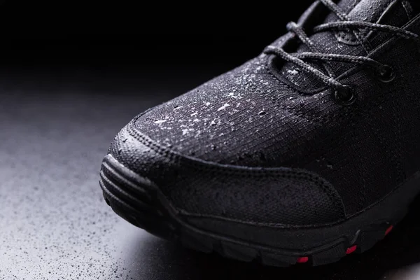 Black mens sneakers with drops of water, close-up on a black isolated background.