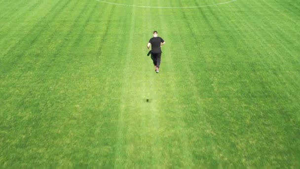 Junger Mann auf dem Fußballplatz mit einem Ball. Schüsse aus der Drohne. die Kamera dreht sich um das Objekt. — Stockvideo