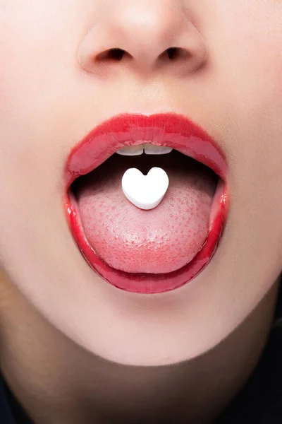 Pastilla en forma de corazón en la lengua. Píldora del amor. La chica se puso una pastilla en la lengua. . — Foto de Stock