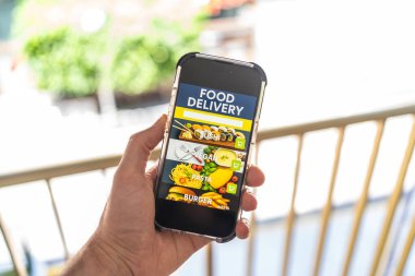 Ekranda yemek dağıtım uygulaması arayüzü olan el ele tutuşan akıllı telefon, suşi, vegan, makarna ve hamburger kategorilerini gösteriyor.