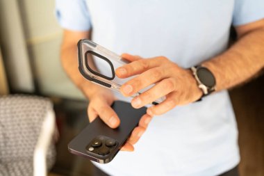 Elinde akıllı telefon ve şeffaf koruyucu bir çanta olan bir adamın, davayı telefona bağlamaya hazırlandığı yakın plan..