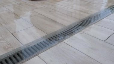 Çamurlu kaldırımda duran yağmur suyuyla tıkanmış yol gideri. Su, yetersiz drenaj sistemi bakımı nedeniyle birikir..