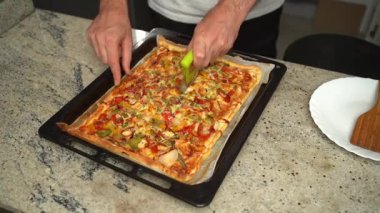 Ev yapımı sebzeli pizza, fırın tepsisinde pizza bıçağıyla dilimleniyor..