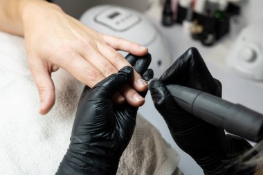 Manikür ameliyatı olan bir adamın yakın çekimi. Siyah eldivenli bir tırnak teknisyeni tırnaklarına dikkat çekmek için elektrikli çivi matkabı kullanır. Erkek tımarı, hijyen ve profesyonel tırnak bakımını ön plana çıkarır..