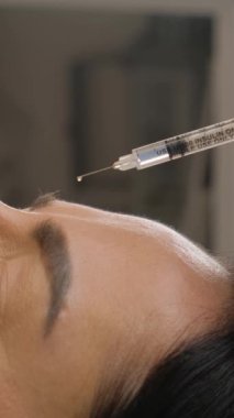 Kozmetik alın enjeksiyonu olan bir kadının yakın çekimi. Siyah eldivenli bir profesyonel, modern estetik, cilt bakımı ve yaşlanmayı önleyici çözümleri vurgulayan bir şırınga ile güzellik tedavi prosedürü uygular..
