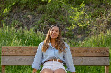 Tahta bankta oturan genç bir kadın gözleri kapalı gülümsüyor huzur dolu pozitiflik ve gerçeklik sağlıklı yaşam tarzı veya ilham verici marka görselleri için idealdir..