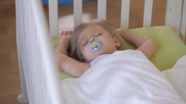 ein kleines Mädchen schläft in einem Babybett mit Schnuller im Mund