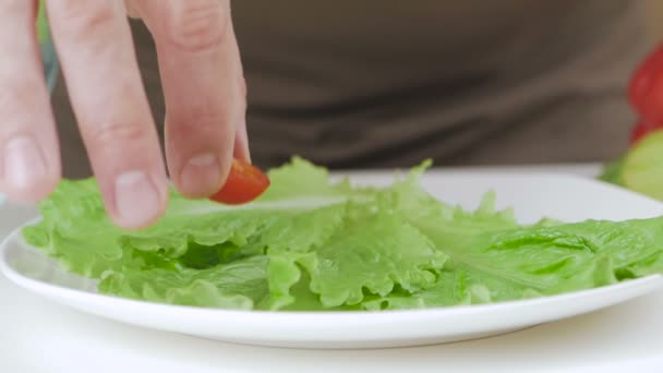Nahaufnahme einer Männerhand, die Hälften von Kirschtomaten auf Salatblättern in einen Teller legt.