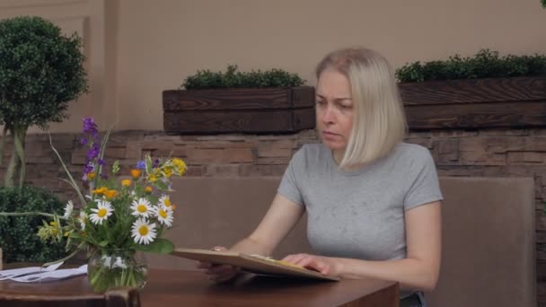 Egy nő étlapot olvas, miközben egy asztalnál ül az étterem nyári teraszán.