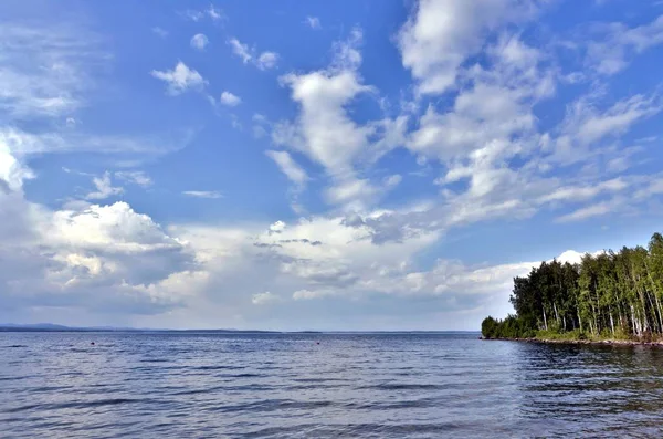 Vue sur le ciel bleu sur le lac avec de beaux nuages plumeux et cumulonimbus par une journée ensoleillée, loin, vous pouvez voir les montagnes de l'Oural — Photo