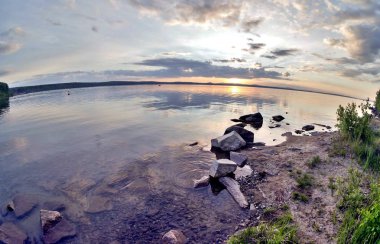 göl üzerinde akşam gökyüzü, bulutlar siluetleri güneş tarafından orman kaplı, kayalık gölün kıyısında aydınlatılmış