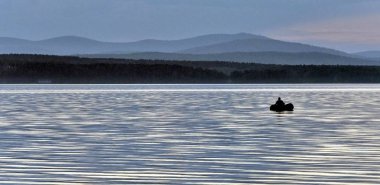 gri-mavi göl ve gökyüzü, yalnız bir balıkçı uzaktan bir teknede akşam Ural Dağları, Güney Urallar, göl Uvildy siluetleri görebilirsiniz