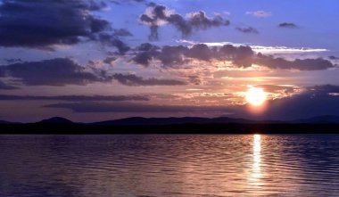 göle siluetleri güneş tarafından aydınlatılmış bulutların üzerinde akşam gökyüzü güneş ufukta ayarlar.