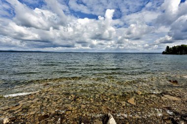 berrak su güneş tarafından aydınlatılmış Gölü, kayalık altında beyaz bulutların göl üzerinde görebilirsiniz