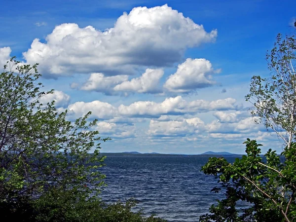 Темно-синее небо с белыми кучевыми облаками над утренним озером — стоковое фото