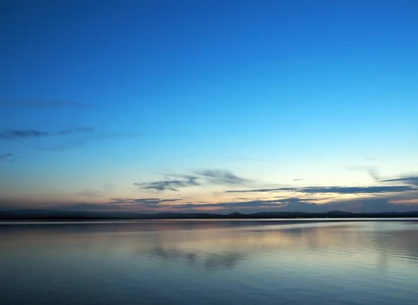 Céu azul do por do sol sobre o lago com nuvens fumegantes claras sobre o horizonte — Fotografia de Stock