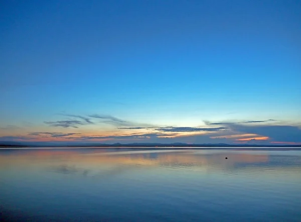 Céu azul do por do sol sobre o lago com nuvens fumegantes claras sobre o horizonte — Fotografia de Stock