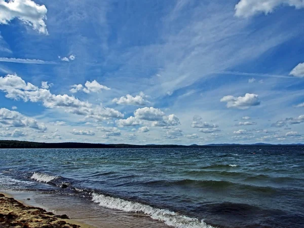 Темно-синє небо з білими кумулонами над ранковим озером — стокове фото