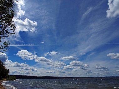 Koyu mavi gökyüzü ile beyaz kümülonimbus bulutları sabah gölünün üzerinde