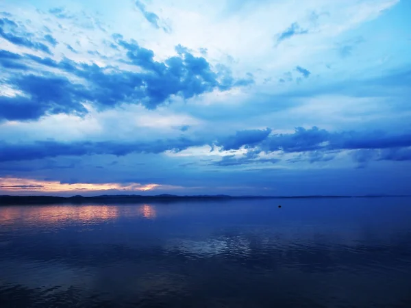 湖面上蔚蓝的夕阳天空，地平线上弥漫着淡淡的烟云 — 图库照片