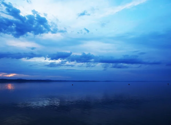 Голубое небо заката над озером с легкими дымчатыми облаками над горизонтом — стоковое фото