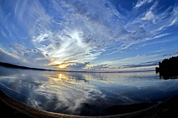 Блакитне небо заходу сонця з мальовничими хмарами відбивається в спокійному озері — стокове фото