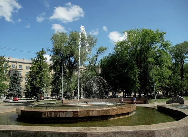 Fontana funzionante nella piazza della città in una giornata calda contro il cielo blu, gocce d'acqua volanti — Foto Stock