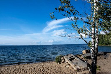 Göl kıyısında bir yaz günü mavi gökyüzü ve ışık bulutlarıyla, Uvildy Gölü