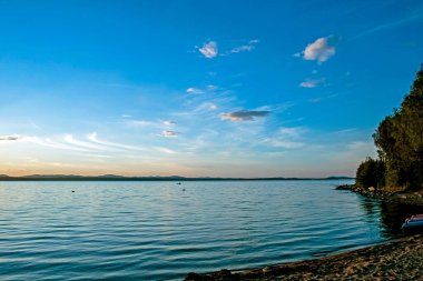 Gölün üzerinde hafif bulutlar olan renkli akşam gökyüzü