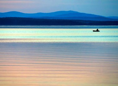 Gölün üzerinde sakin mavi günbatımı gökyüzü, bir balıkçı teknesinin silueti, suyun sakin yüzeyi, Uvildy Gölü, Güney Urallar