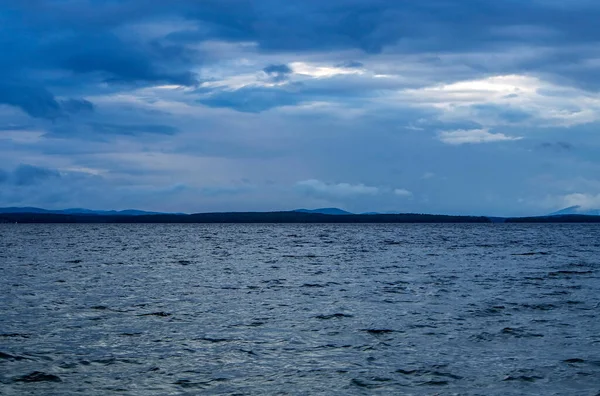 dark overcast sky over the lake on a summer evening, gloomy clouds, the opposite shore in the distance, lake Uvildy, southern Urals