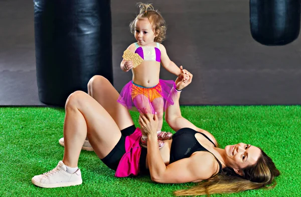 Charming sports mom plays in the gym with her little daughter. Mixed media