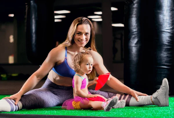 Charming sports mom trains in the gym with her little daughter and a French bulldog. Mixed media