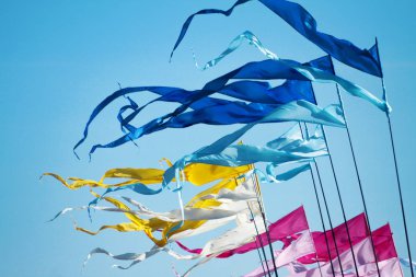 A waving blusky, cyan, yellow, white, pink and rose long triungular flags on a background bright blu sky clipart