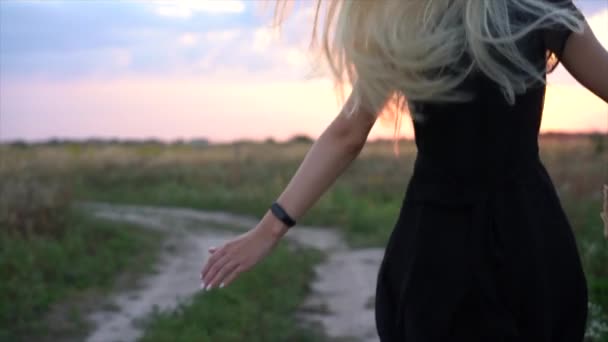 Menina bonita em vestido preto corre através do campo ao pôr do sol. A menina corre em direção ao pôr-do-sol através do campo. Movimento lento — Vídeo de Stock