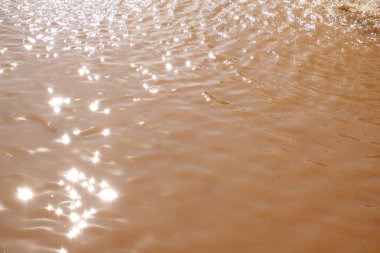 Su yüzeyinde küçük dalgalar ve güzel yansımalar ışığı yansıtır. Kahverengi suyun dokusu. Doğa arka planı, küçük dalgalar, güneş ışığı, duvar kağıdı için manzara, ağ, baskı. Kahverengi su arkaplanı.