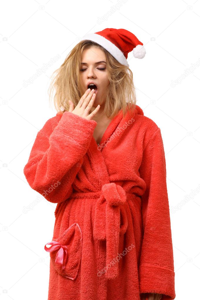 Young sleepy girl in a dressing gown wearing Santa's hat yawns. Wild hair. Wants to sleep. New Year. Christmas. After the holiday. Isolated on white background.