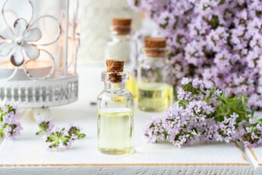 Bir şişe beyaz ahşap zemin üzerinde taze çiçek açan kekik dallar ile uçucu yağ